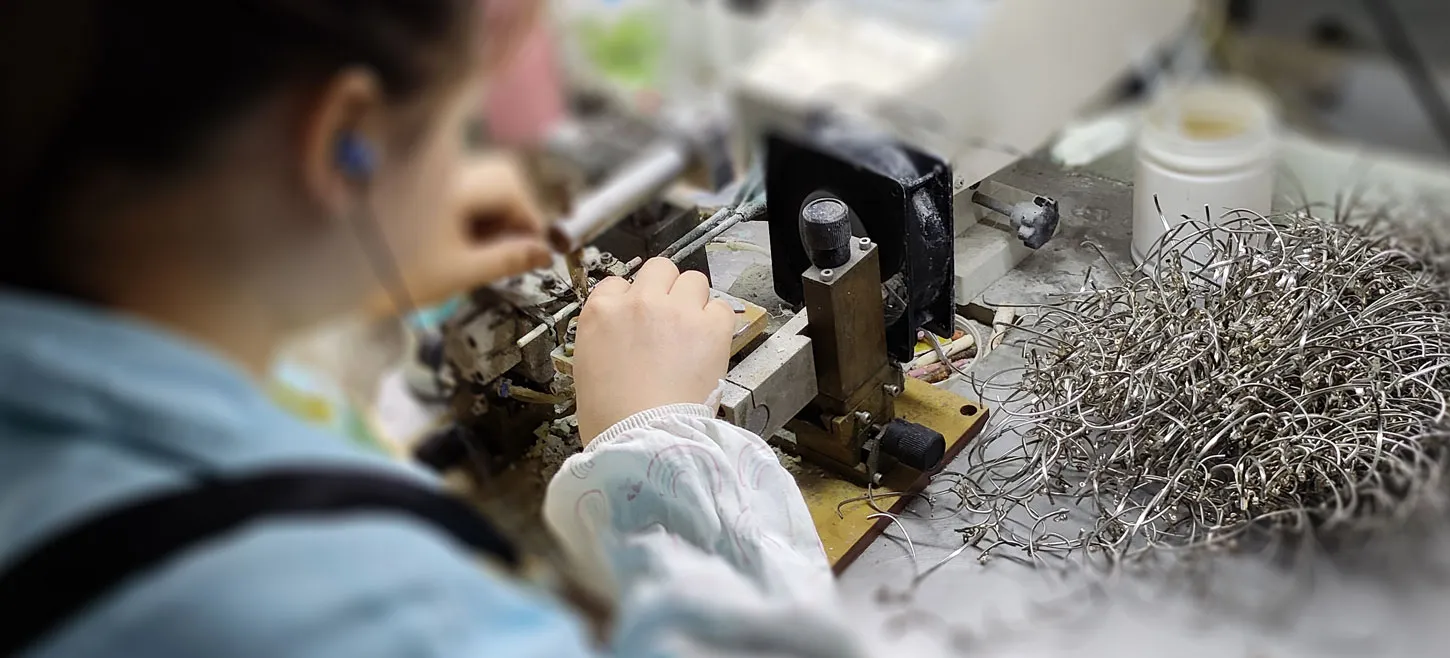 Female worker is welding rim for metal eyewear frames at production line